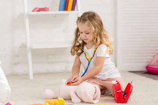чарівна дитина вивчає м'яку іграшку кролика зі стетоскопом у дитячій кімнаті
  - Фото, зображення