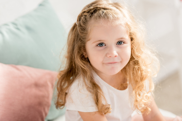 high angle view of adorable kid with curly hair looking at camera in children room - Foto, immagini