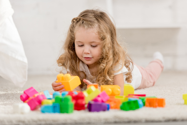 nivel de superficie del niño adorable jugando con el constructor plástico de color en la alfombra en la habitación de los niños
 - Foto, Imagen