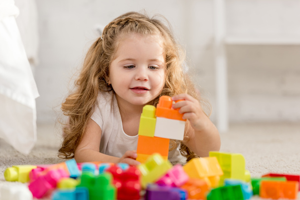 selective focus of adorable kid playing with colored plastic constructor on carpet in children room - Фото, зображення