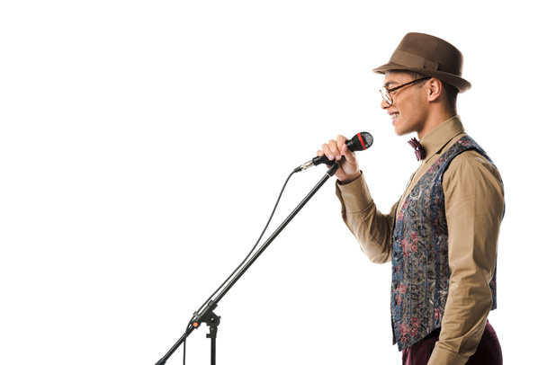side view of smiling mixed race male musician in hat singing in microphone isolated on white - Foto, Imagen