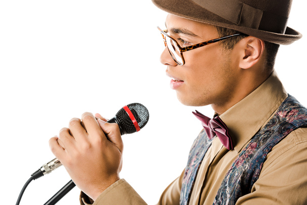 side view of handsome mixed race man in hat singing in microphone isolated on white - Foto, imagen