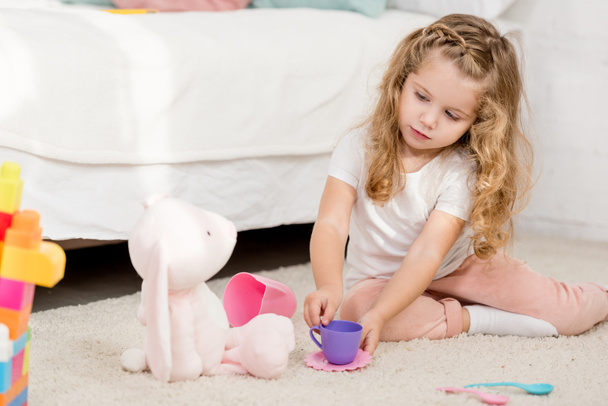 adorable child playing with rabbit toy and plastic cups in children room - Фото, зображення