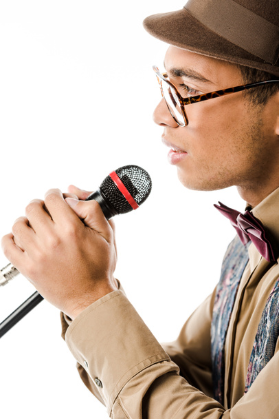 side view of mixed race male musician in hat singing in microphone isolated on white - Foto, Imagem