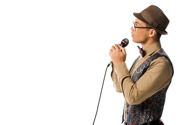 side view of mixed race male musician in hat singing in microphone isolated on white - Foto, afbeelding