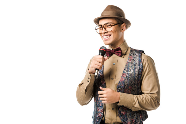 laughing mixed race man in hat and eyeglasses singing in microphone isolated on white - Fotoğraf, Görsel