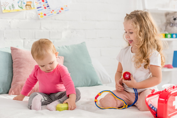 toddler and preschooler sisters playing with first aid kit in children room - Photo, Image
