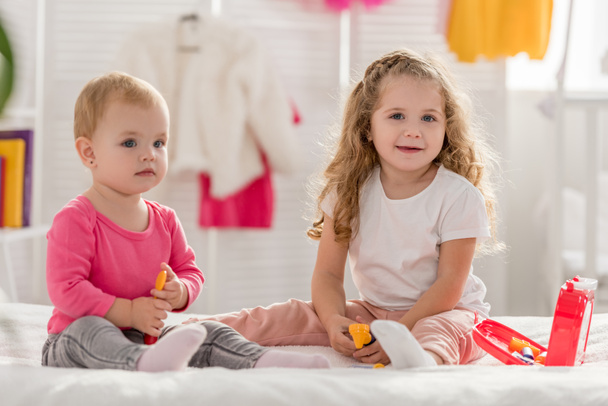 entzückende Schwestern spielen mit Verbandskasten im Kinderzimmer und schauen in die Kamera - Foto, Bild