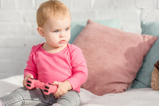 adorable kid in pink shirt holding pink gamepad on bed in children room - Photo, Image