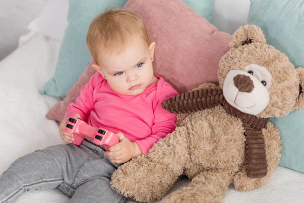 angry adorable kid in pink shirt holding pink joystick on bed in children room - Fotografie, Obrázek