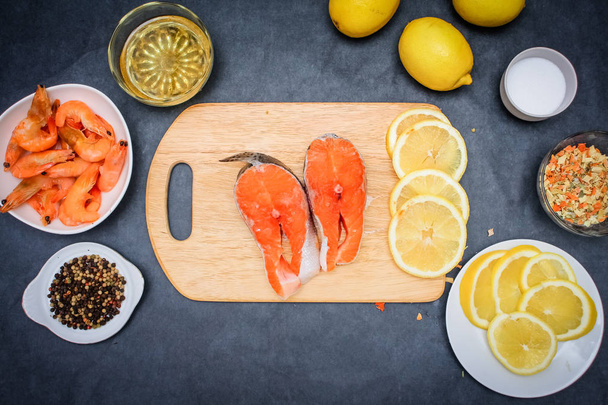 Raw fish with seasonings. Wooden board in the middle of the frame with the salmon laid out in a plate raw shrimp pepper lemon slices with seasoning oil. - Foto, Bild