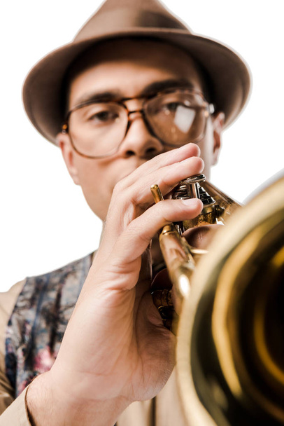 close up view of mixed race male musician in stylish hat and eyeglasses playing on trumpet isolated on white  - 写真・画像