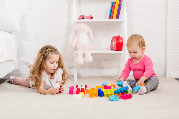 adorable sisters playing with constructor on carpet in children room - Фото, зображення