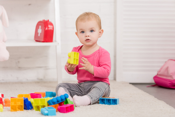 adorable kid playing with constructor on carpet in children room - Foto, afbeelding