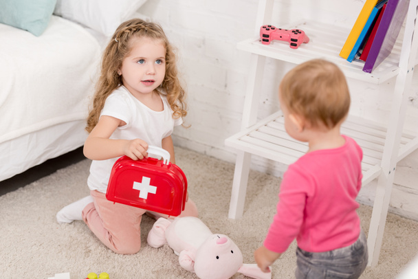 adorable sisters playing with first aid kit in children room - Фото, зображення