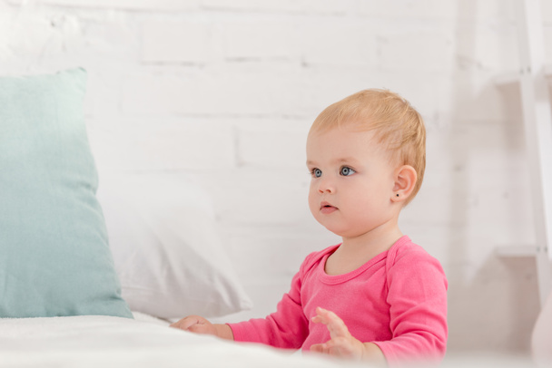 adorable kid leaning on bed and looking away in children room - Photo, Image