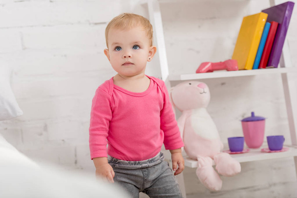 adorable kid in pink shirt standing and looking up in children room - Foto, Bild