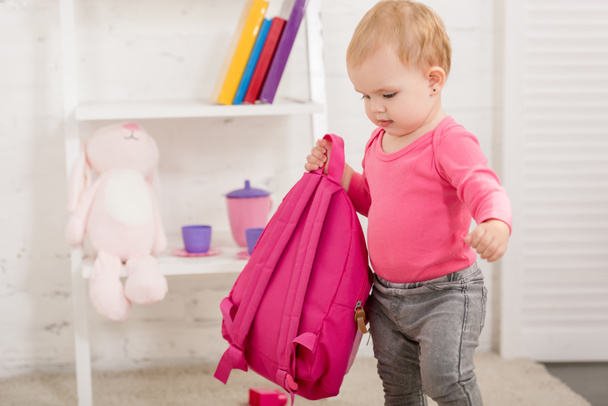adorable kid in pink shirt carrying pink bag in children room - 写真・画像