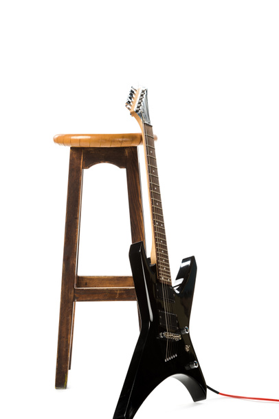 Μαύρη ηλεκτρική κιθάρα κοντά σε ξύλινη καρέκλα που απομονώνονται σε λευκό - Φωτογραφία, εικόνα