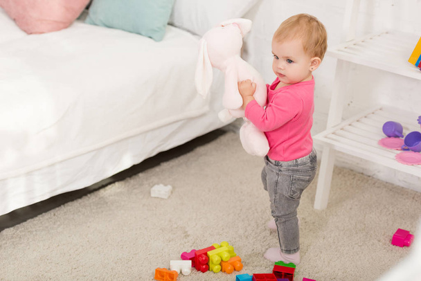 adorable kid in pink shirt holding rabbit toy in children room - Photo, Image