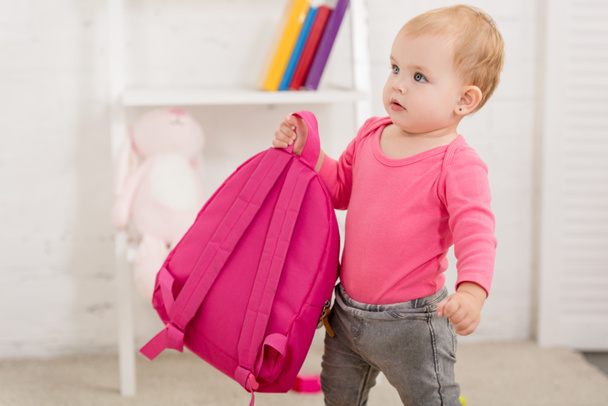 adorable child in pink shirt carrying pink bag in children room - Valokuva, kuva