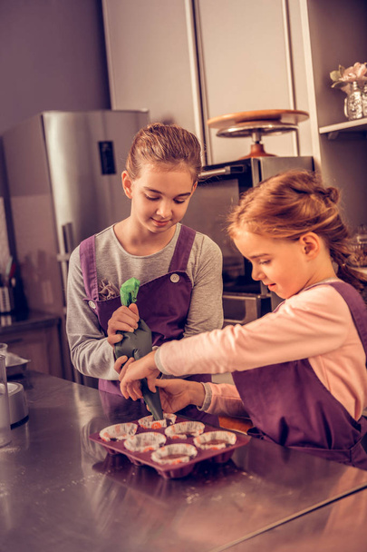 Радісні приємні молоді сестри готують кекси разом
 - Фото, зображення