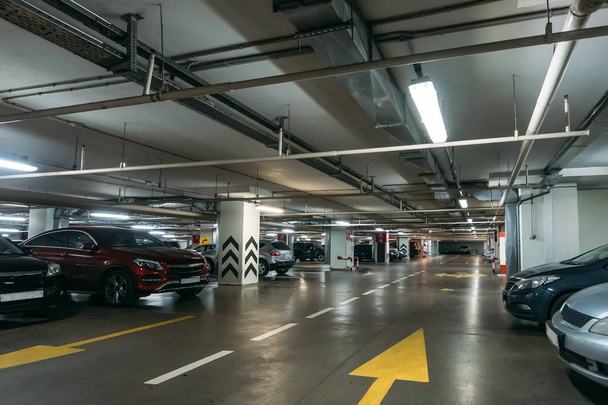 Parking souterrain éclairé intérieur sous le centre commercial moderne avec beaucoup de véhicules et des flèches sur le sol
 - Photo, image