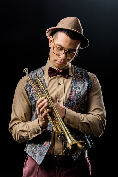 музыкант смешанной расы, позирующий с трубой, изолированный на черном
 - Фото, изображение