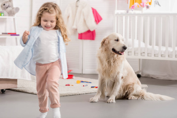 cheerful adorable kid and golden retriever in children room - Photo, Image