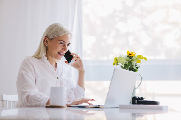 Vrouw praten over de telefoon, met behulp van de laptop. Werken vanuit huis, freelancen, online baan. - Foto, afbeelding
