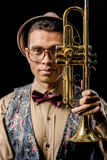 Porträt eines stilvollen jungen männlichen Musikers, der mit Trompete isoliert auf schwarz posiert - Foto, Bild