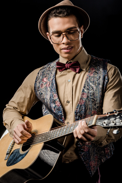 mladý muž hudebník brýle a klobouk, hraje na akustickou kytaru, samostatný na černém - Fotografie, Obrázek