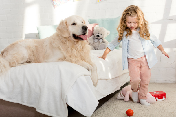 adorable niño de pie cerca de la cama con perro en la habitación de los niños
 - Foto, Imagen
