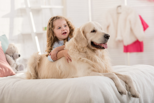 adorable kid and dog lying on bed in children room - Photo, Image
