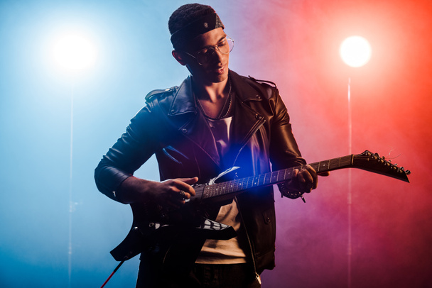 músico masculino tocando la guitarra eléctrica en el escenario con humo e iluminación dramática
  - Foto, imagen