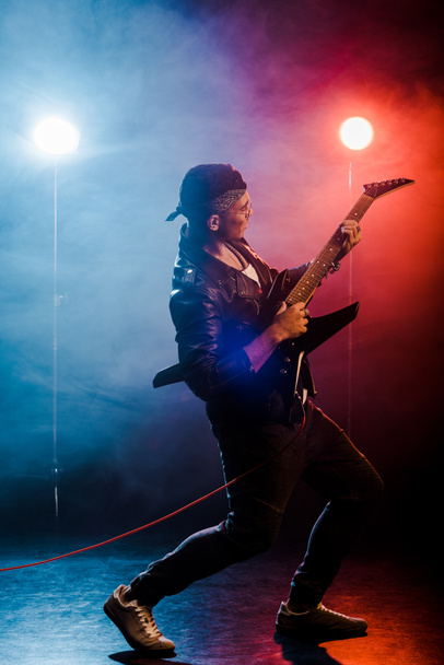 giovane musicista di sesso maschile che suona la chitarra elettrica sul palco con fumo e illuminazione drammatica
  - Foto, immagini