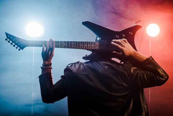 rear view of male musician in leather jacket playing on electric guitar behind head on stage - Foto, Imagem