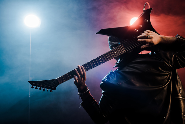 vue arrière du musicien masculin en veste de cuir jouant à la guitare électrique derrière la tête sur scène
  - Photo, image