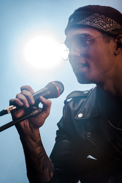 όμορφος αρσενικό ροκ μουσικός τραγουδώντας στο μικρόφωνο στη σκηνή με τα φώτα της δημοσιότητας - Φωτογραφία, εικόνα