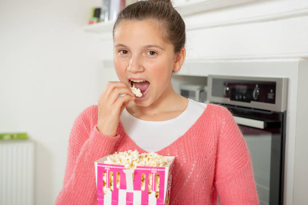 young teenage girl with a pink sweater eating popcorn at home - Фото, изображение