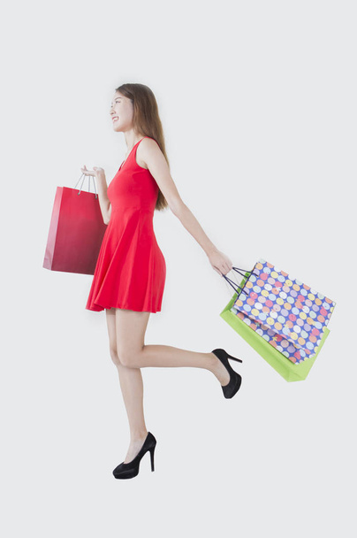 Giovane donna che indossa un vestito rosso che tiene alcune borse e sorride guardando altrove
, - Foto, immagini