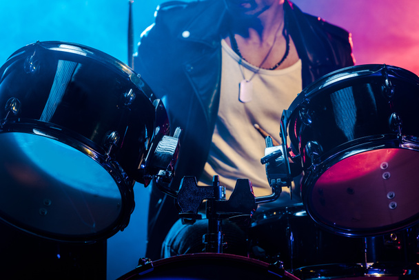 Oříznout záběr mužské hudebník hrající na bubny během rockový koncert na jevišti s kouřem a dramatické osvětlení - Fotografie, Obrázek