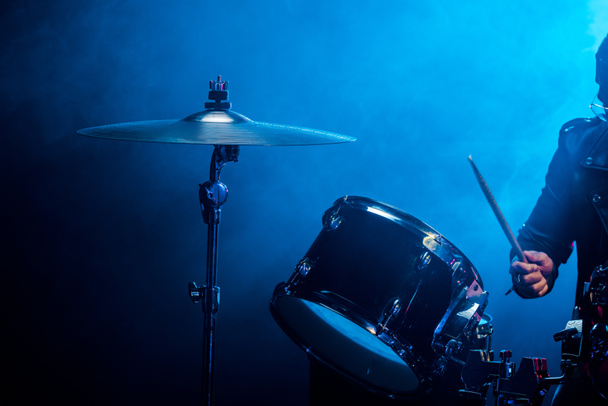 vista parcial del músico masculino tocando la batería durante el concierto de rock en el escenario con humo e iluminación dramática
 - Foto, imagen