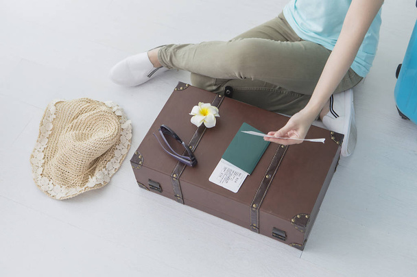 Young woman sitting on the floor next to a suitcase and a hat, passport with tickets - Foto, afbeelding
