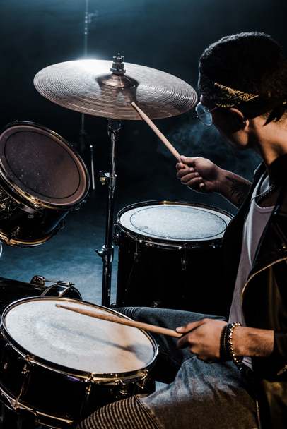 vista lateral de la raza mixta músico masculino tocando la batería durante concierto de rock en el escenario
  - Foto, Imagen