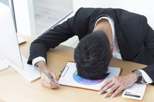 Νεαρός άνδρας σε ένα κοστούμι που είναι ξαπλωμένος στο γραφείο - Φωτογραφία, εικόνα