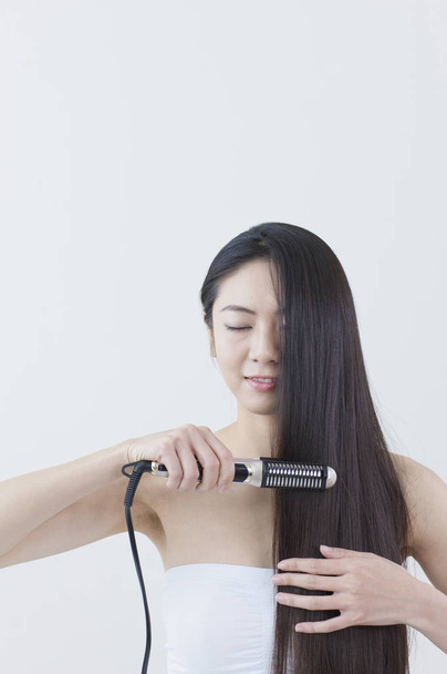 Young Asian woman smiling ironing her hair - Foto, imagen
