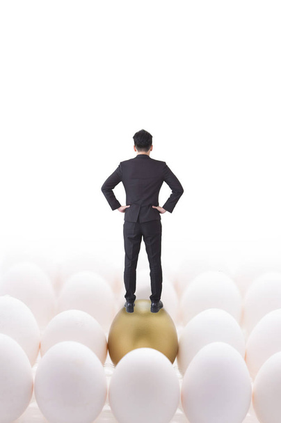 Young Asian man wearing a suit standing on an golden egg and showing his back to the camera - Photo, Image