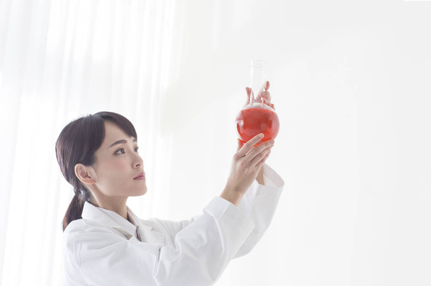 Young female doctor holding up a red test tube and looking at it - Photo, image