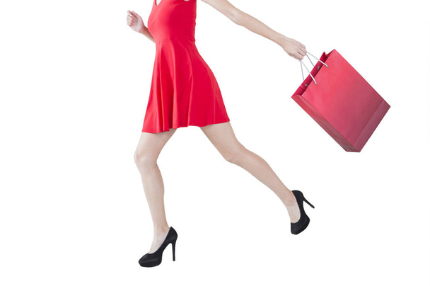 Νεαρή γυναίκα, φορώντας ένα κόκκινο φόρεμα, κρατώντας μια σακούλα και τρέξιμο - Φωτογραφία, εικόνα